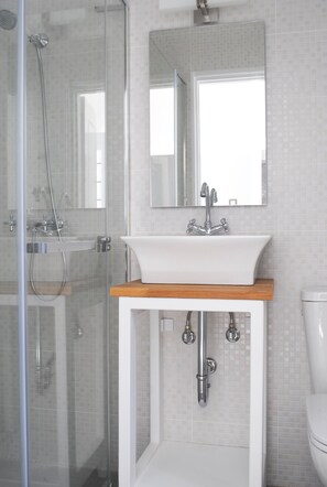 A bathroom with a glass-enclosed shower, a white sink with a wooden countertop, and a mirror above the sink.