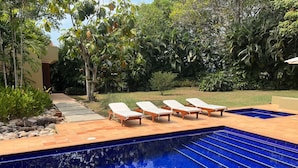 Una piscina circondata da vegetazione lussureggiante e un vialetto in pietra, con quattro lettini.