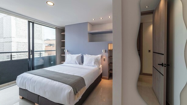 A modern bedroom with a large bed, built-in shelving, and a view of the city. - w Elegant 3BR w Outdoor Balcony (Medellín)