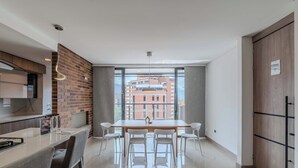 A modern kitchen with a brick accent wall, a dining area with a large window, and a view of a building outside. - w Elegant 3BR w Outdoor Balcony (Medellín)