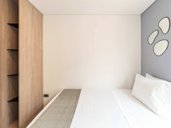 A modern bedroom with a bed, a wooden wardrobe, and a gray accent wall with decorative mirrors.