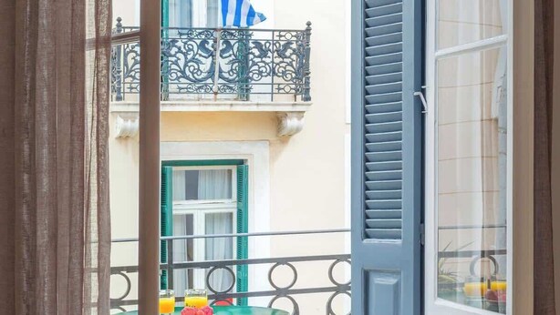 A balcony with a table and chairs, a window with blue shutters, and a flag. - Athens Residence Cozy Suite Near Acropolis (Athens)