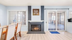 A living room with a fireplace, a dining table with chairs, and a large window with blinds. - Perfect Family Getaway w Garden Near ONT Airport (Ontario)