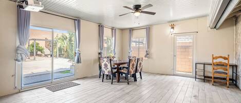 A spacious room with a ceiling fan, a projector, a dining table with chairs, and a wooden chair.