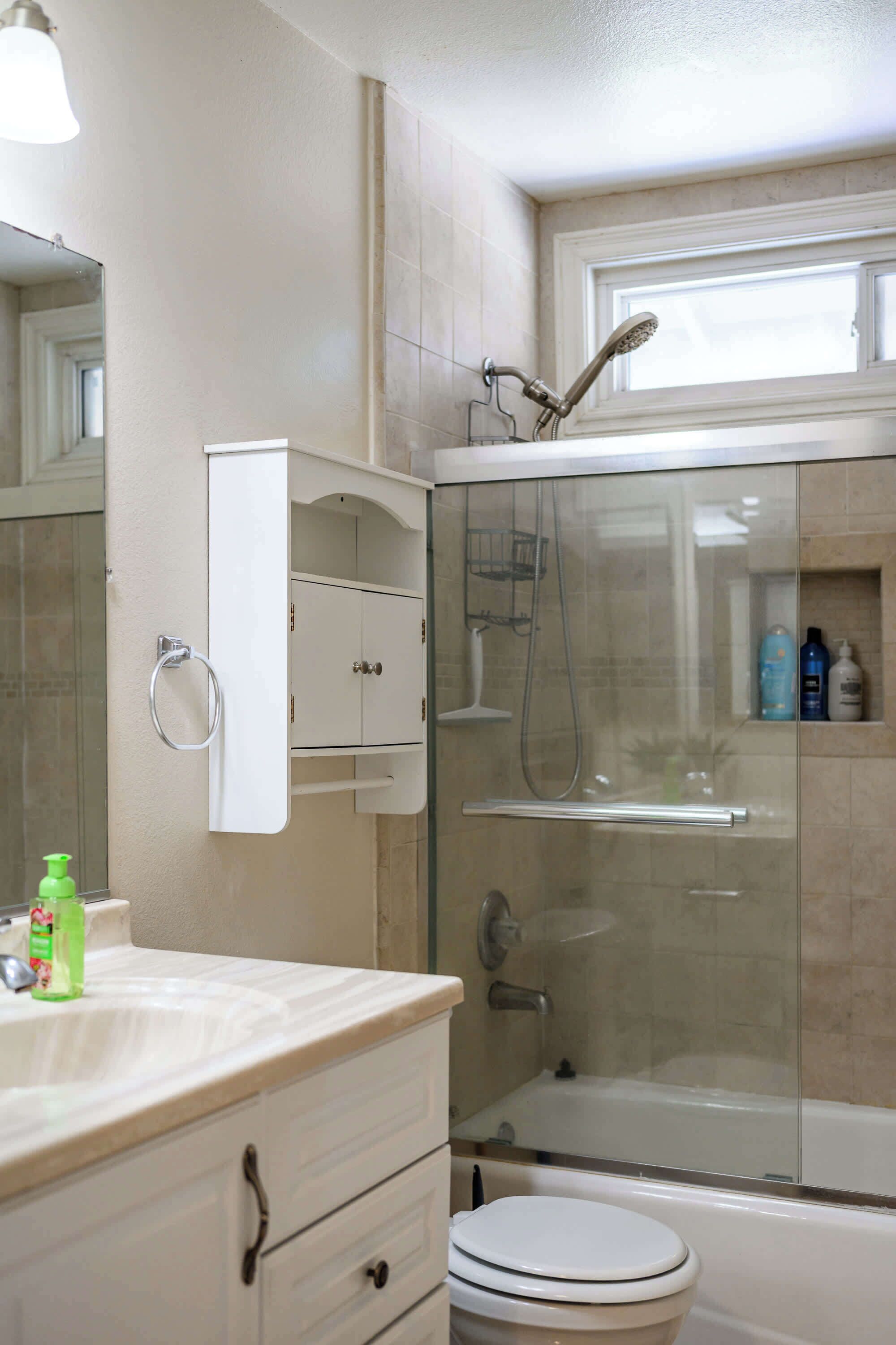 Un bany amb dutxa de vidre, un vàter blanc i un lavabo amb mirall.