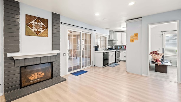 A modern living room with a fireplace, a kitchen area, and a dining space. - Perfect Family Getaway w Garden Near ONT Airport (Ontario)