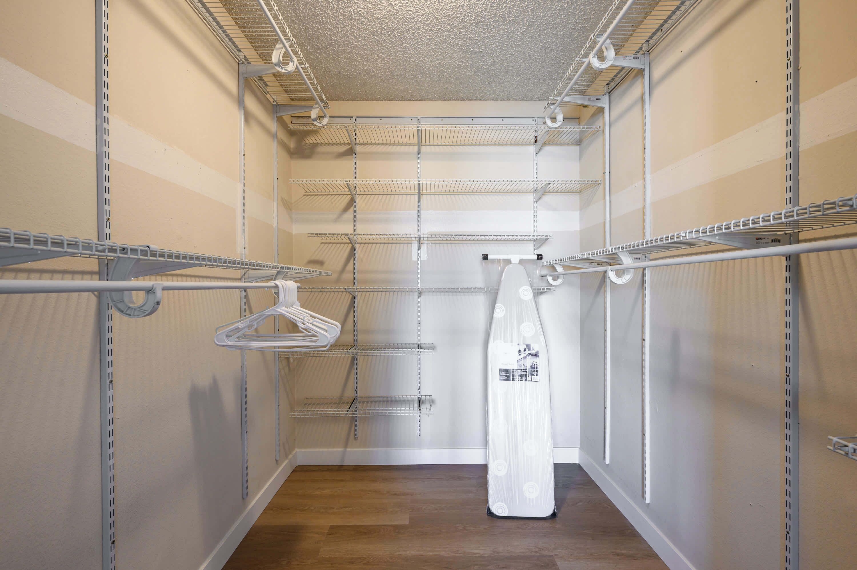A walk-in closet with multiple shelves and hanging space, featuring a wooden floor and white walls.