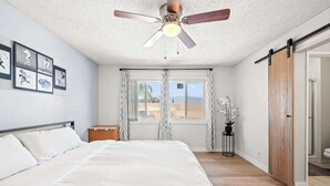 A bedroom with a bed, ceiling fan, window with curtains, and a view of the beach. - Perfect Family Getaway w Garden Near ONT Airport (Ontario)