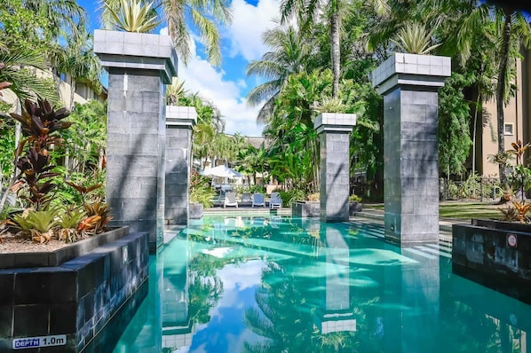 Una piscina con agua cristalina, rodeada de palmeras y una estructura de piedra.