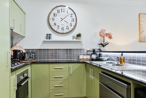 Una cocina con gabinetes verdes, un reloj blanco y negro, una cafetera y un fregadero.