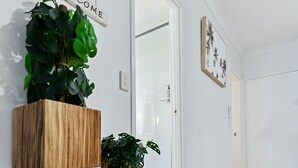 A hallway with a white door, a welcome sign, and two wooden planters with green plants. - Family Friendly 2BR Apartment with Resort Pool (Westcourt)
