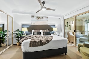 Un dormitorio moderno con una cama grande, un ventilador de techo y vista a la playa a través del ventanal.
