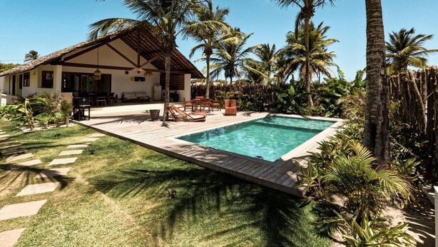 Una casa con piscina circondata da palme e un prato curato.