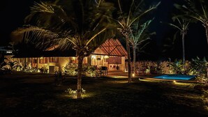 Una località turistica ben illuminata con piscina, palme e una grande casa con tetto rosso.