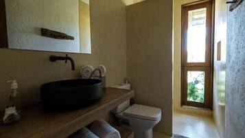 A bathroom with a wooden vanity, black sink, white toilet, and a window with a view of greenery.