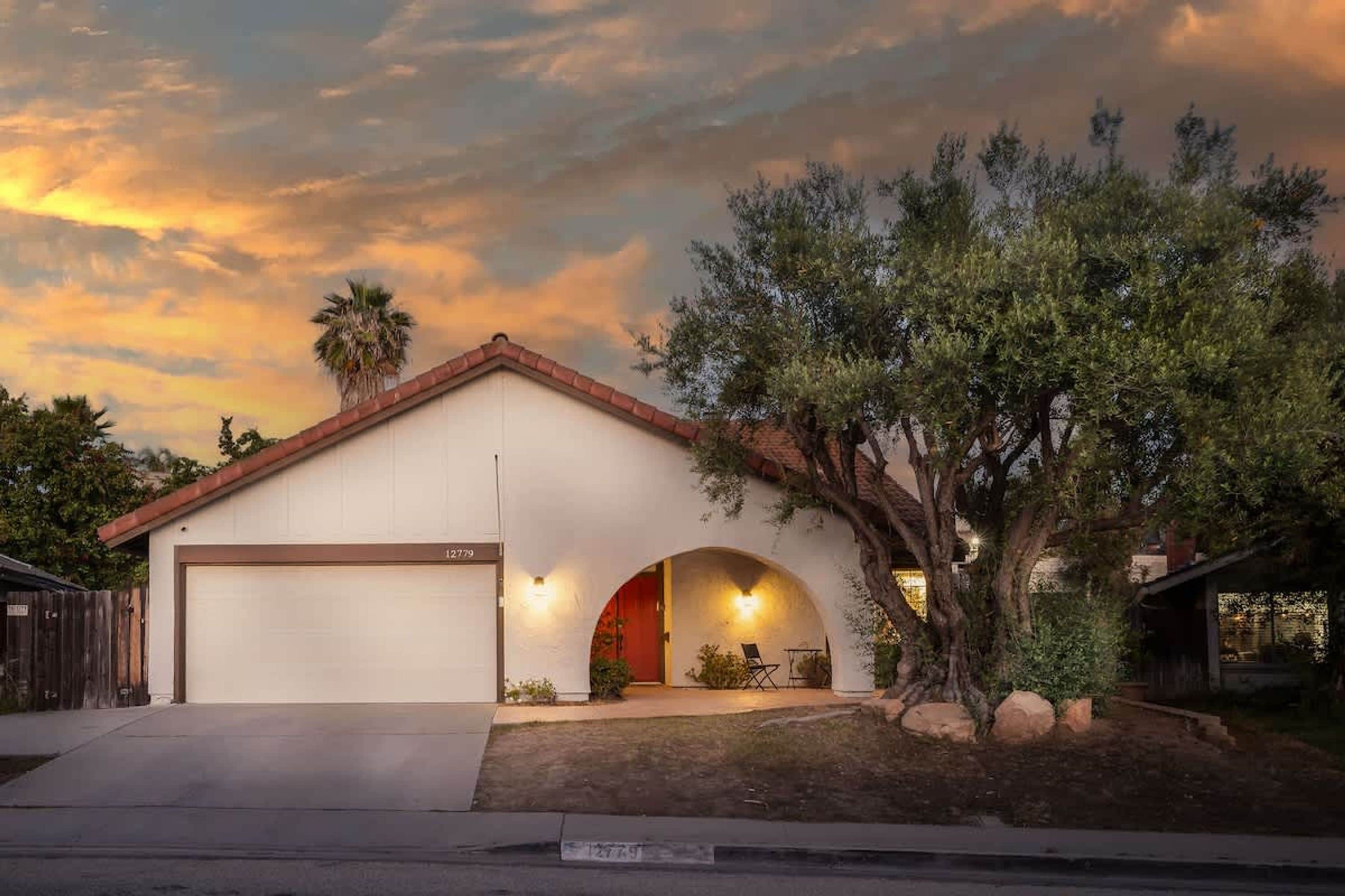 A single-story house with a garage, a covered patio, and a tree in the front yard.