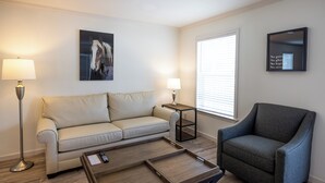 A living room with a sofa, armchair, coffee table, floor lamp, and wall art.