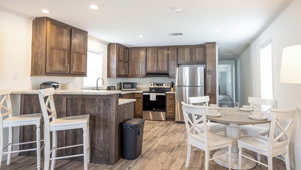 A modern kitchen with wooden cabinets, a central island, white bar stools, and a dining table with chairs.