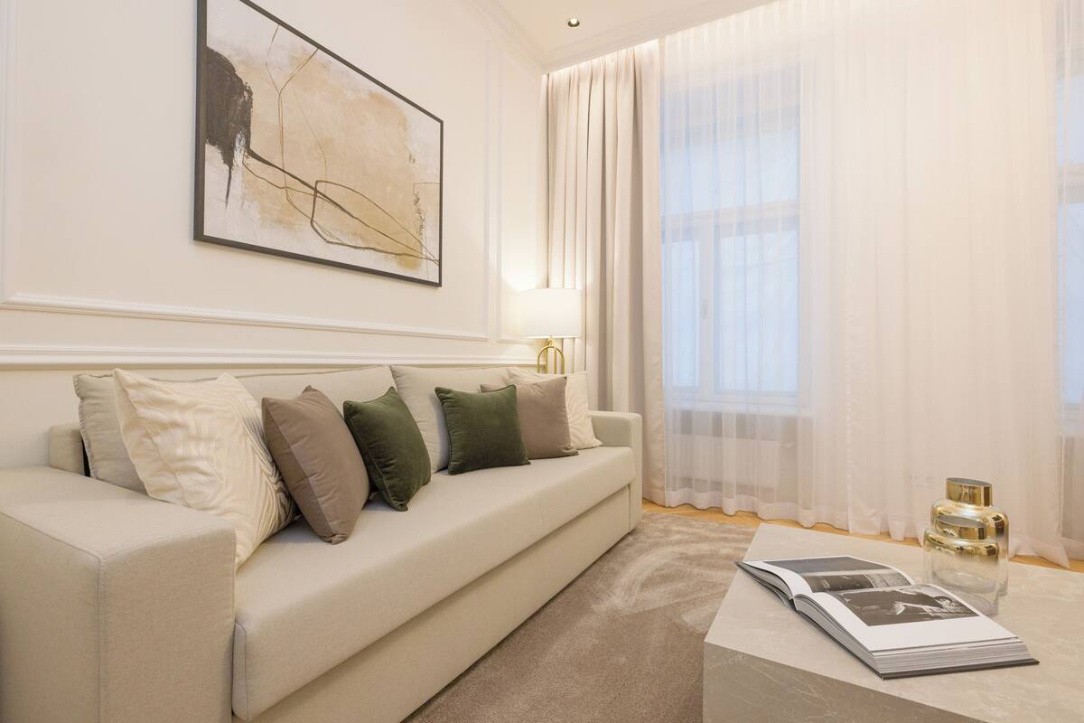 A modern living room with a beige sofa, a coffee table, and a large window with sheer curtains.
