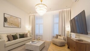 A modern living room with a sofa, a coffee table, a TV, and a chandelier. - RAFAEL KAISER - Signature Apartments  (Vienna)