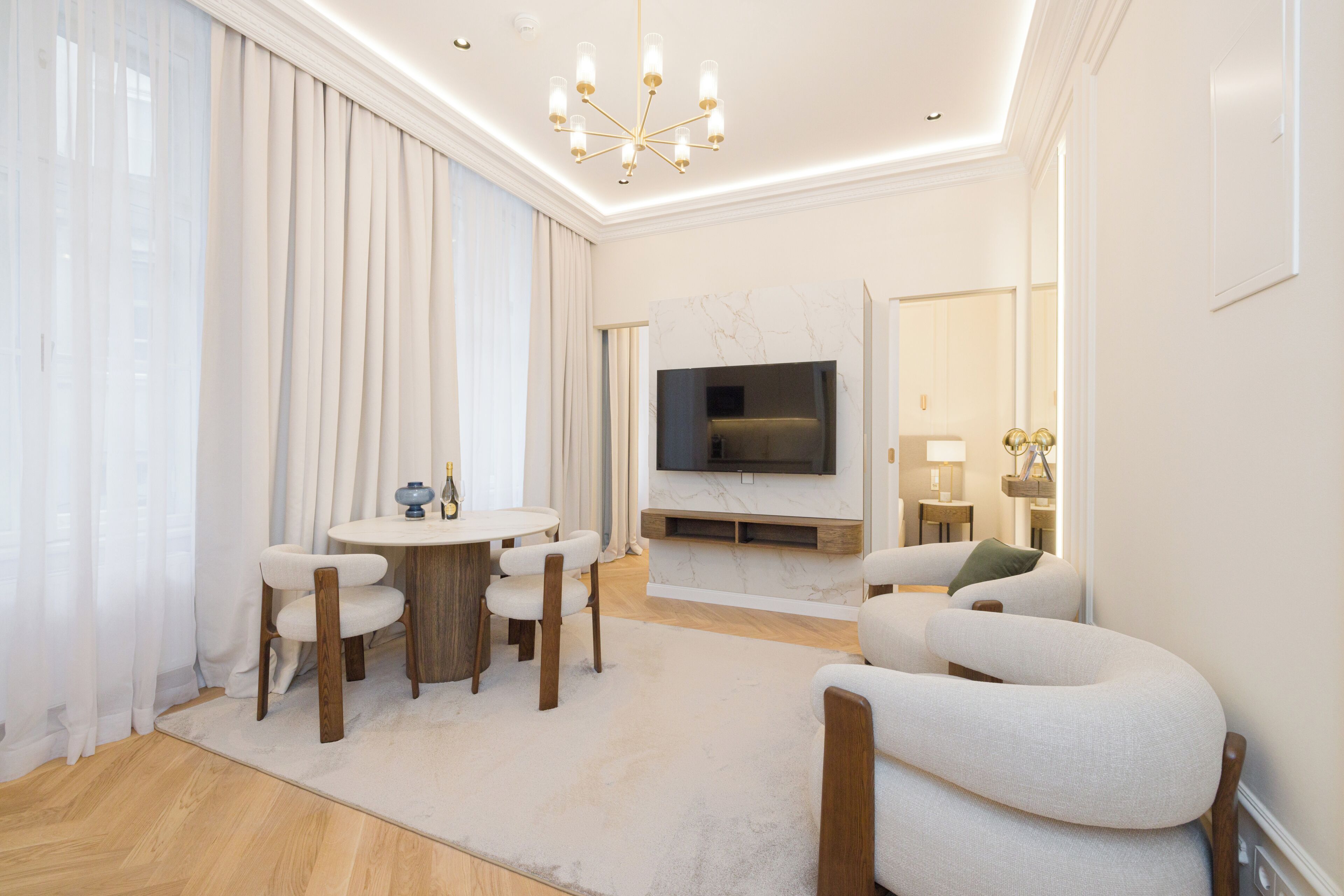 Een moderne woonkamer met een ronde eettafel, twee banken, een flatscreen televisie en een kroonluchter.