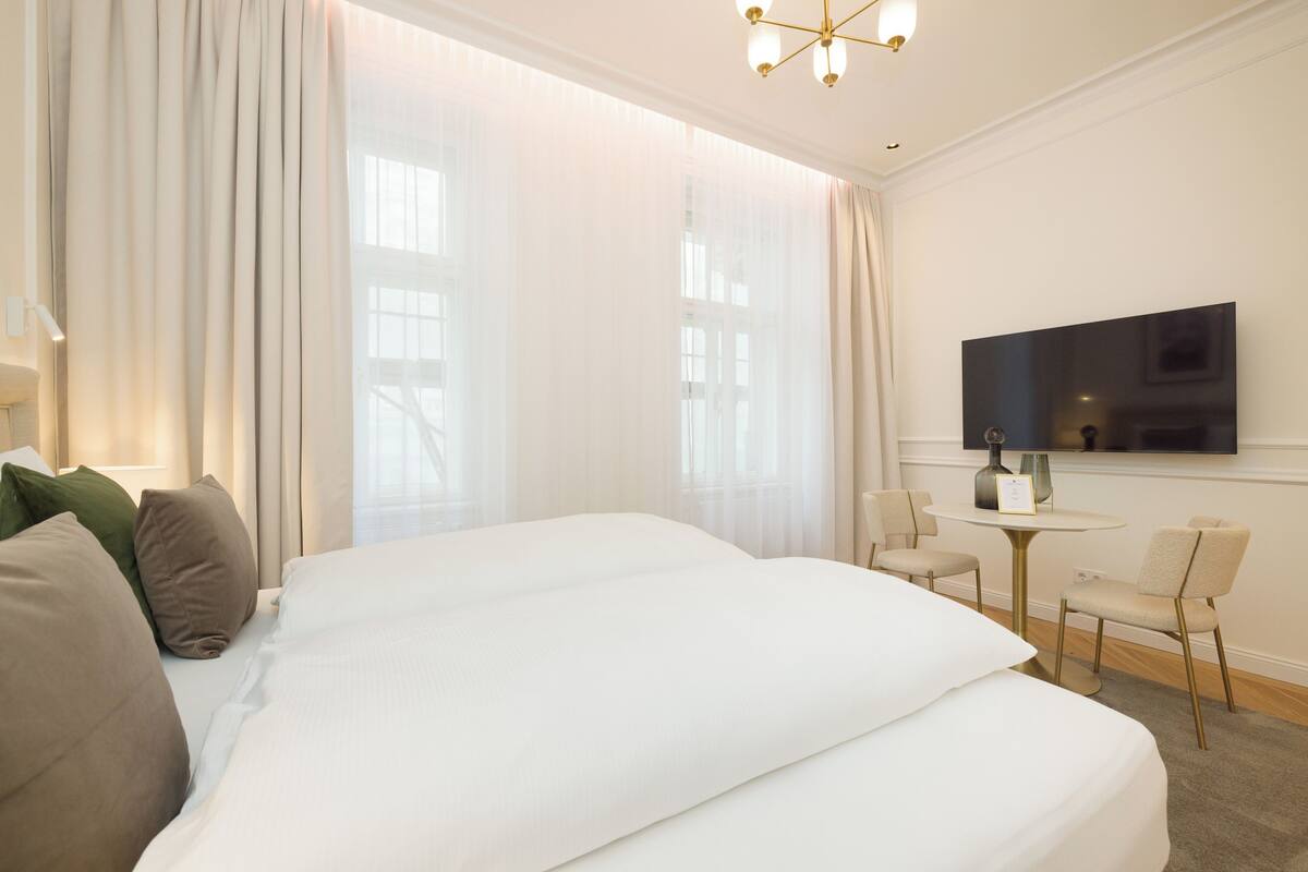 A hotel room with a large bed, a TV mounted on the wall, a small round table, and two chairs.
