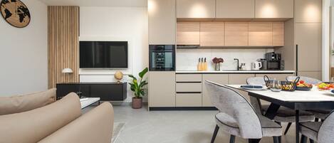 A modern kitchen with a dining area, a flat-screen TV, and a potted plant.