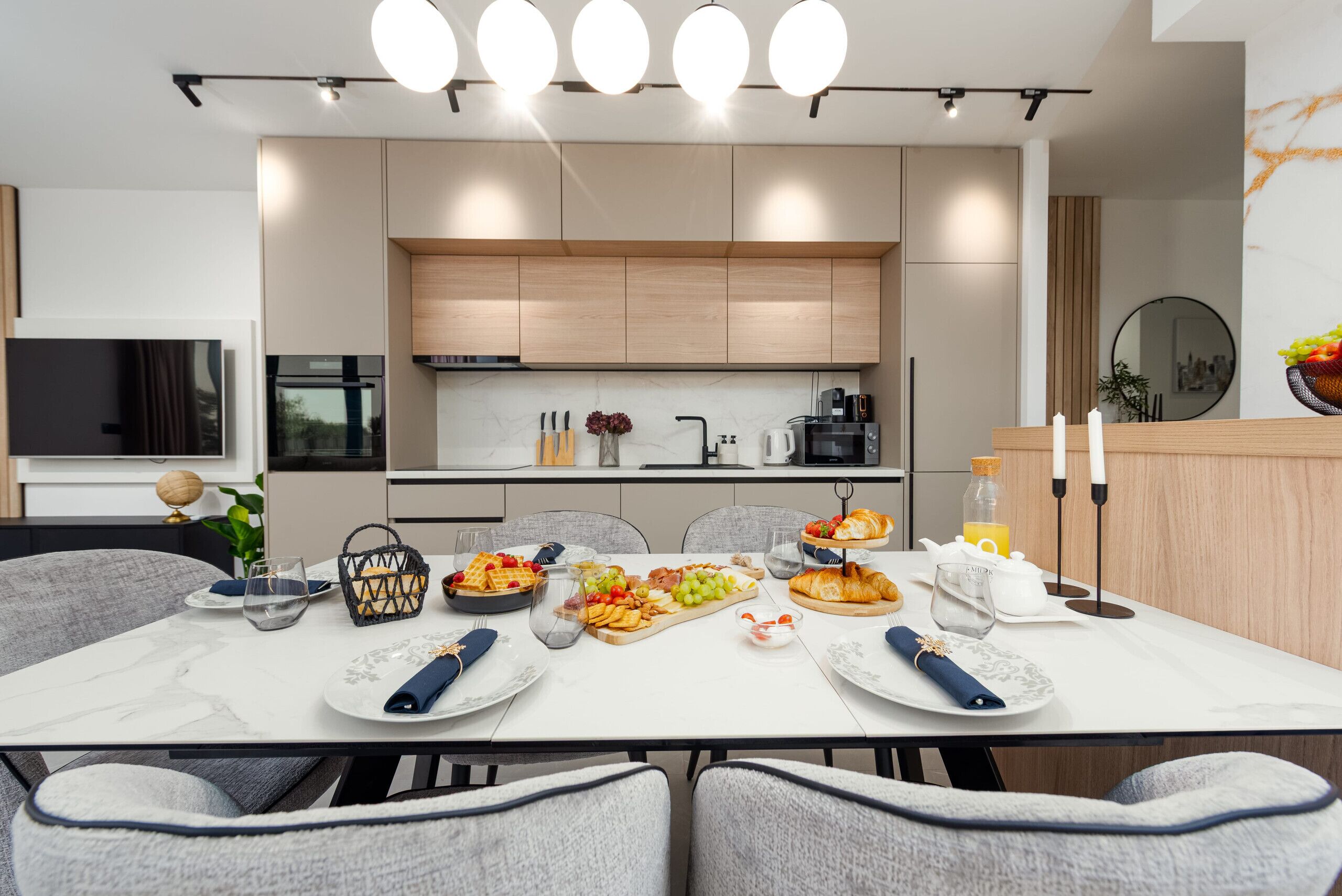 A modern kitchen with built-in appliances, a dining area with a marble table, and a breakfast spread.