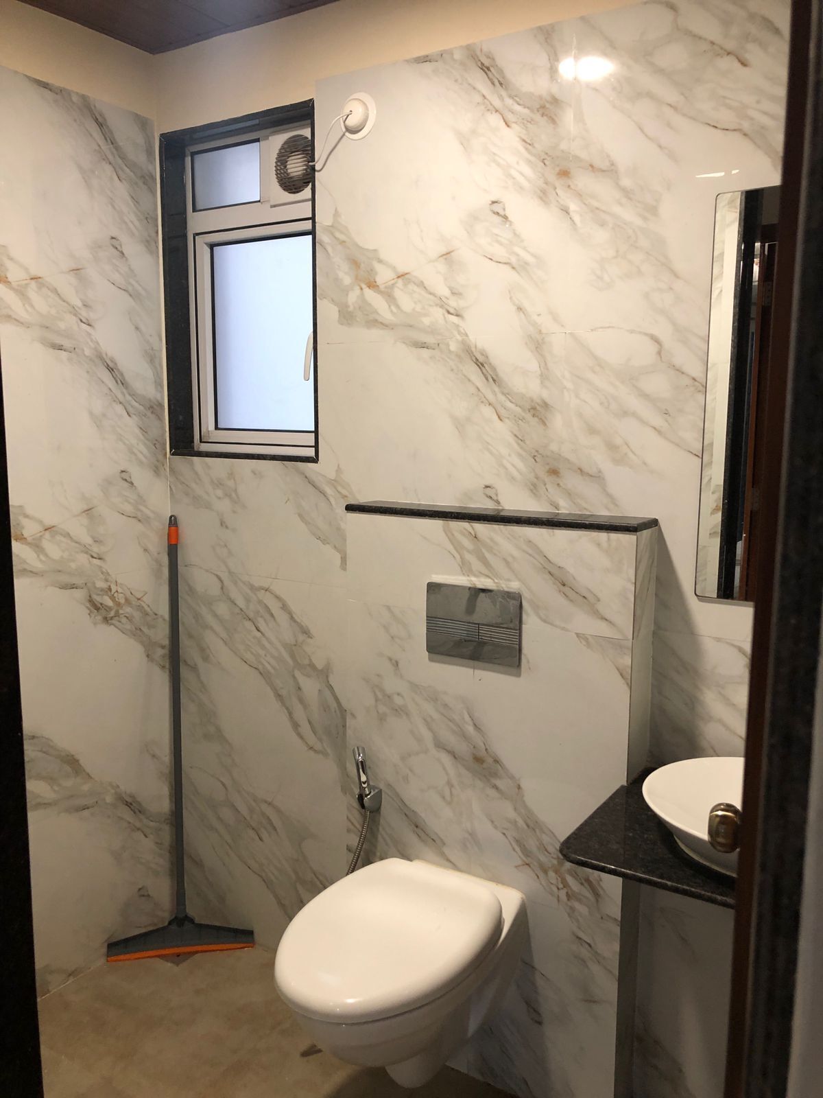 A bathroom with a marble wall, a window, a shower, and a toilet.