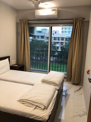 Habitación de hotel con dos camas, aire acondicionado, ventana con cortinas y vistas a edificios y zonas verdes.