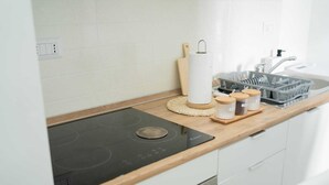 A kitchen with a black induction cooktop, a wooden cutting board, a paper towel holder, a dish rack, and a small wooden table with jars.