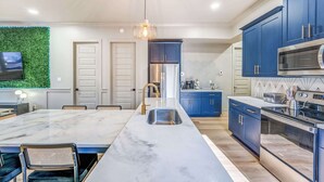 A modern kitchen with a marble island, blue cabinets, stainless steel appliances, and a green wall accent.