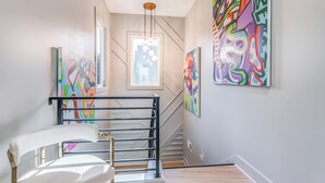 A staircase with a black railing, a white chair, and colorful abstract paintings on the walls.