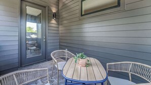 A covered patio with a round table and wicker chairs, a potted plant, and a sliding glass door.