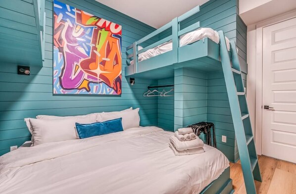 A bunk bed room with teal walls, a colorful abstract painting, and a white door.