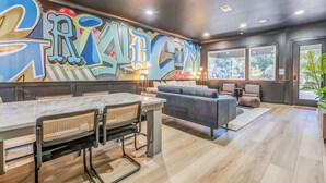 A modern interior with a graffiti wall, a dining area with a marble table, and a grey sofa.