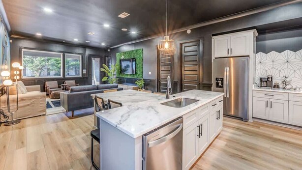 A modern kitchen with a marble island, stainless steel appliances, and a dining area with a sofa and table.