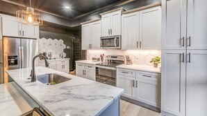 A modern kitchen with white cabinets, a stainless steel refrigerator, a microwave, and a large island with a sink.
