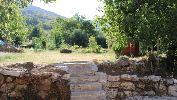 A stone staircase leading up to a rustic building surrounded by greenery and hills.