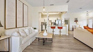 Un soggiorno moderno con un divano bianco, un tavolino da caffè e, sullo sfondo, una zona cucina.