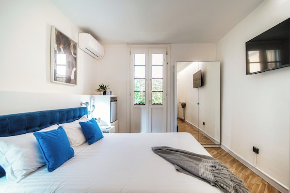 A bedroom with a large bed, a flat-screen TV mounted on the wall, and a door leading to another room. - Cosy apt near Duomo di Como (Como)