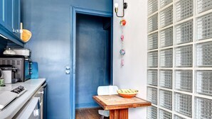 A compact kitchen with a blue door, a white sink, a small table with a bowl, and a wall with patterned glass panels.