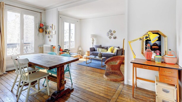 A spacious living area with a wooden dining table, chairs, a sofa, and a desk with drawers.