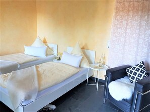 Quarto de hotel com duas camas, uma mesa redonda pequena, uma cadeira e cortina decorativa.
