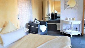 A hotel room with a bed, a chair, a small table, a mirror, and a shelf with bottles. - Room 'Hortensie' with Private Terrace, Private Garden and Wi-Fi (Weil der Stadt)