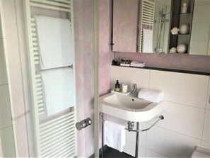 Casa de banho com cabine de duche em vidro, lavatório branco com uma toalha e um espelho acima do lavatório.