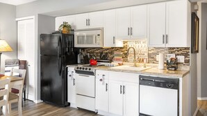 A modern kitchen with white cabinets, a black refrigerator, a microwave, a stove, and a dishwasher. - Fisherman's Lure (Branson)