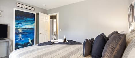 A bedroom with a large bed, a night sky painting, a door, and a small table with a bottle and glasses.