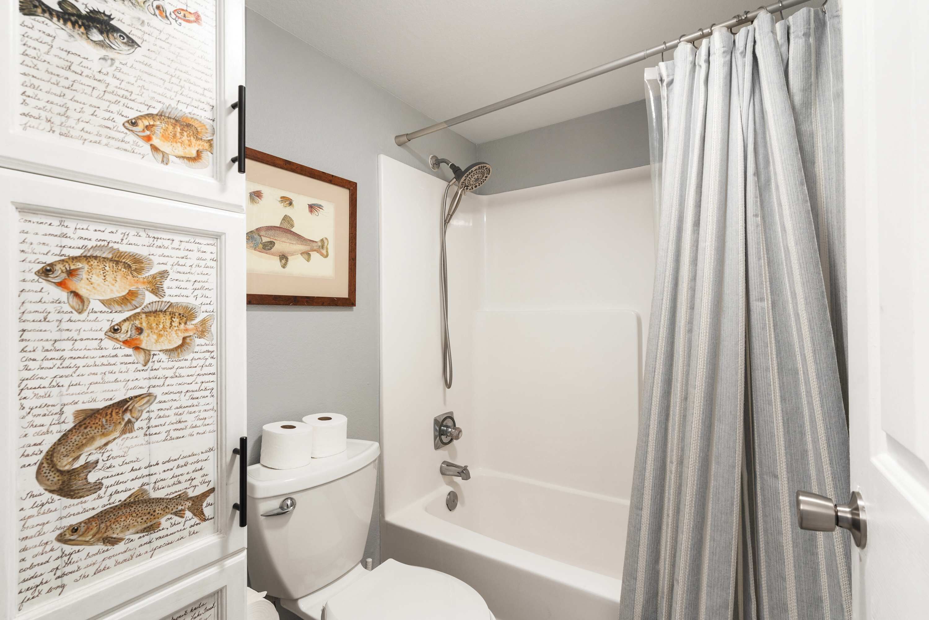 Een badkamer met een bad, toilet en afbeeldingen van vissen in lijsten aan de muur.