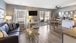 A modern living room with a sofa, coffee table, and a TV. There is a dining area with a table and chairs, and a kitchen area with a counter and appliances. - Fisherman's Lure (Branson)